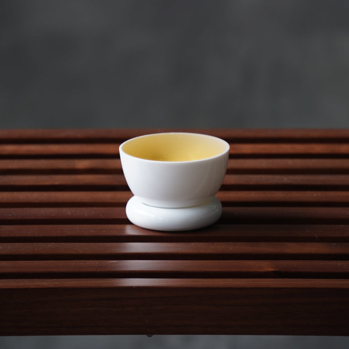 圓好夢白瓷茶杯盛裝金黃茶湯，圓形杯托置於深色木格茶盤