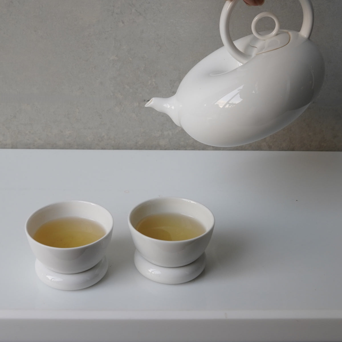 圓好夢白瓷茶壺斟茶情境，茶湯注入兩只置於圓形杯托上的茶杯
