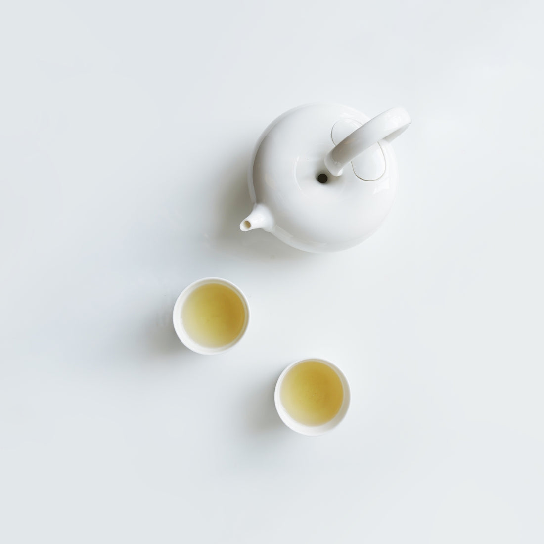 圓好夢白瓷茶壺與兩只茶杯俯視圖，純白茶器盛裝金黃色茶湯