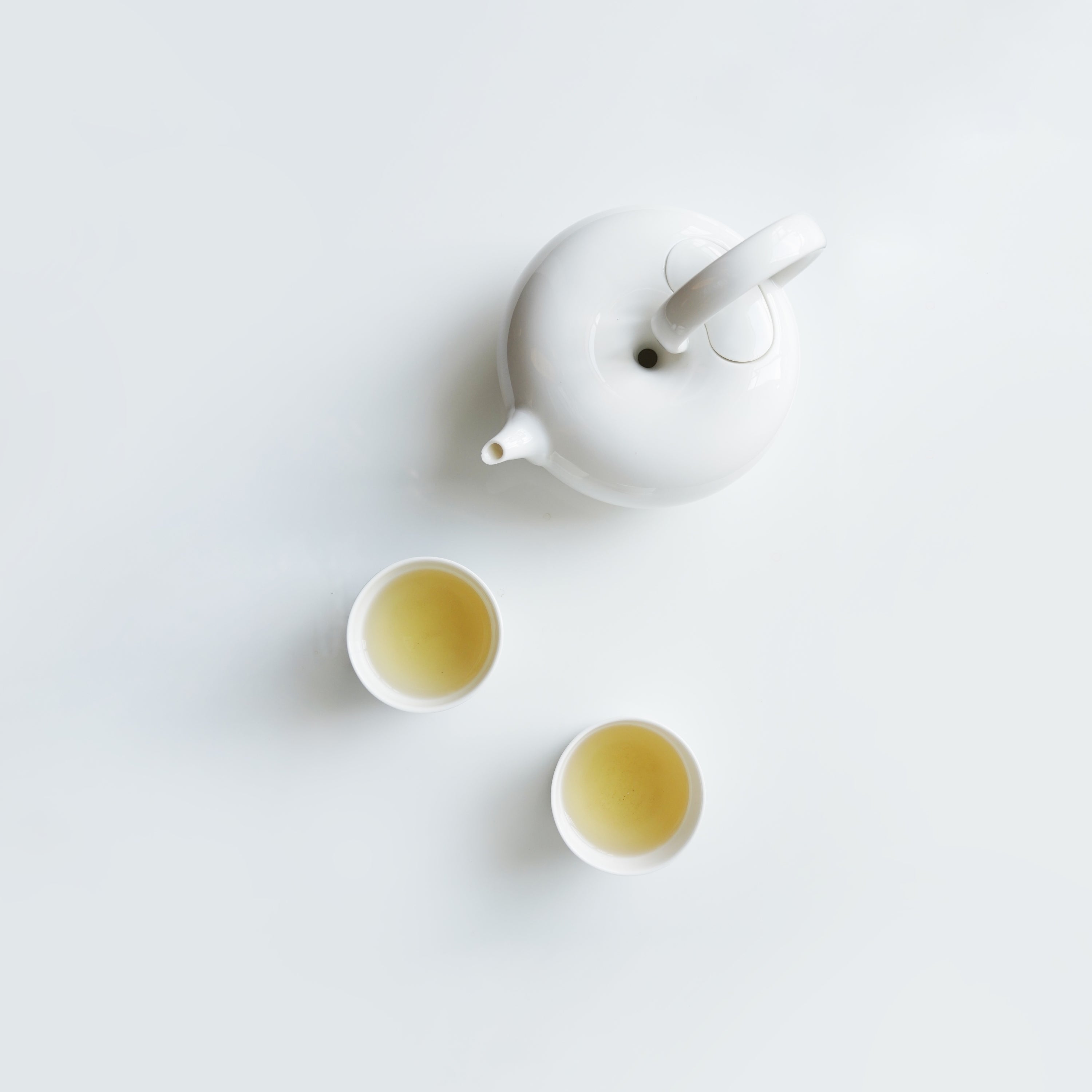 圓好夢白瓷茶壺與兩只茶杯俯視圖，純白茶器盛裝金黃色茶湯
