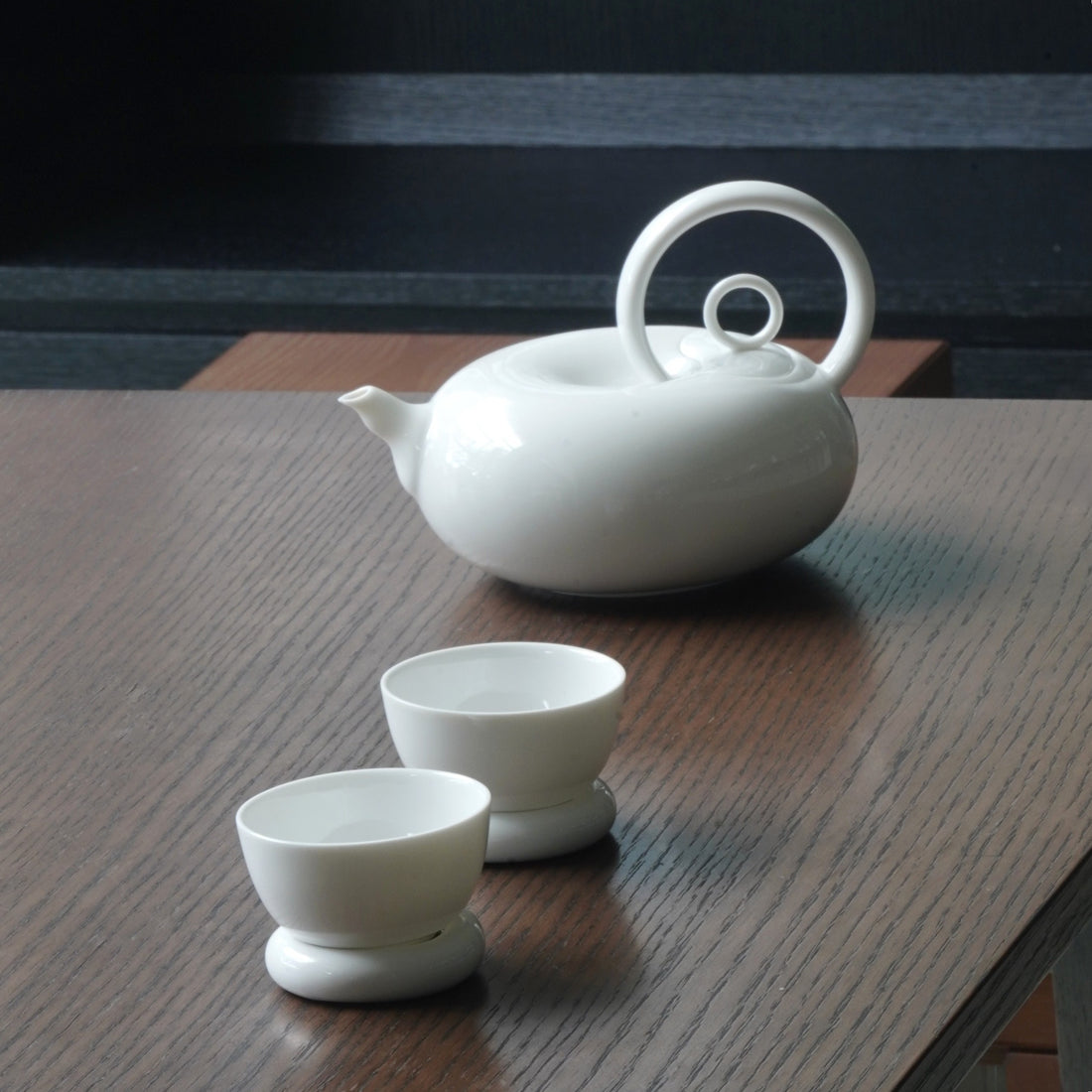 圓好夢白瓷茶具一壺兩杯組，渾圓壺身與環形把手陳列於深色木質茶桌