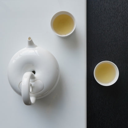 圓好夢白瓷茶具俯視構圖，圓形茶壺跨越明暗桌面並搭配兩只品茗杯