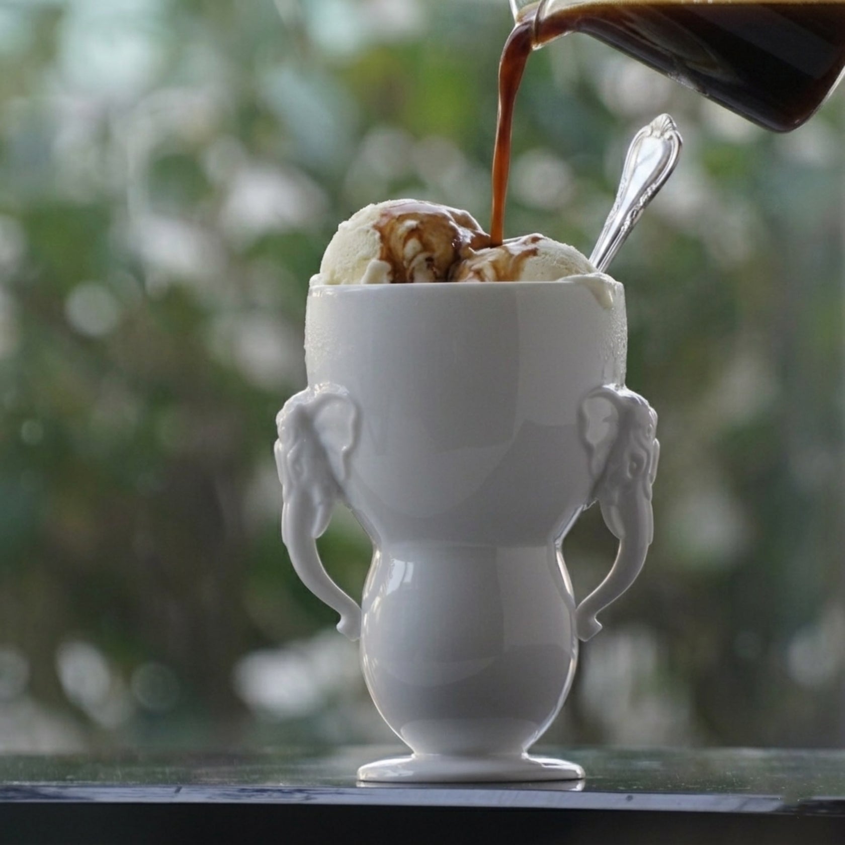 萬象一新精緻的雙象耳白瓷杯，完美盛裝上一份經典的義式甜點 Affogato（阿芙佳朵）濃郁、高溫的 Espresso 緩緩澆淋在冰涼細緻的香草冰淇淋上，沿著瓷器優雅的弧度流淌，展現出冷與熱、黑與白的極致交融。