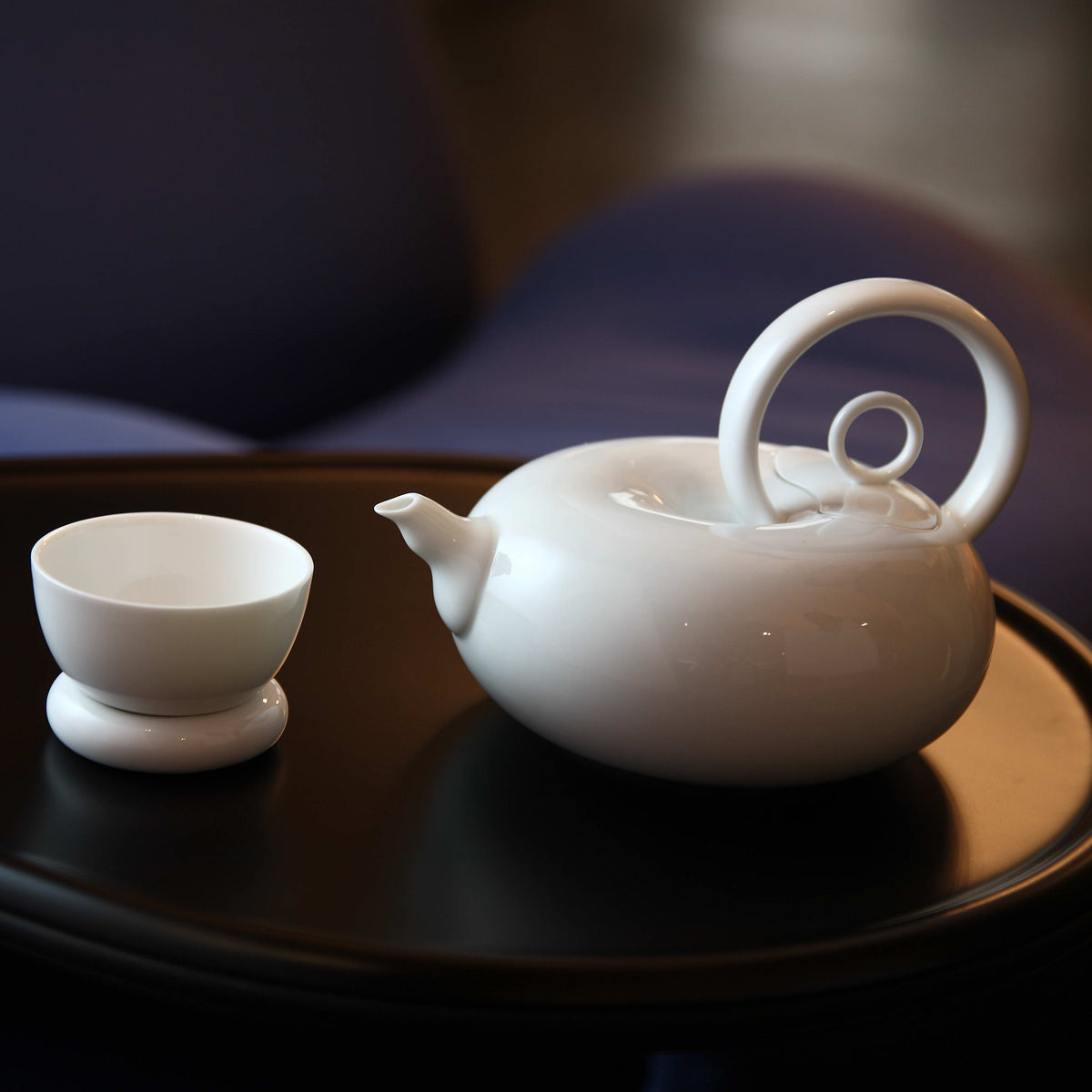 圓好夢一壺一杯白瓷茶具，環形把手與渾圓壺身陳列於深色圓盤